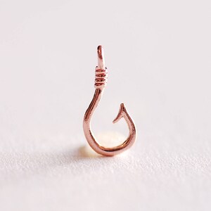 May include: A rose gold fish hook charm pendant. The hook is made of metal and has a shiny finish.
