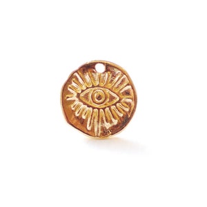 May include: Gold-toned metal charm with an embossed eye design. The eye is surrounded by radiating lines.