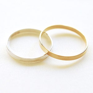 May include: Two simple wedding bands, one gold and one silver, are intertwined on a white background.