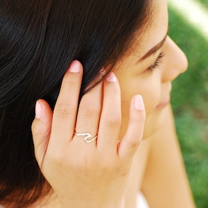 Puede incluir: Una mujer con el pelo largo y oscuro lleva un anillo de plata en forma de ola en su dedo. El anillo es un diseño sencillo con una línea curva que se asemeja a una ola.