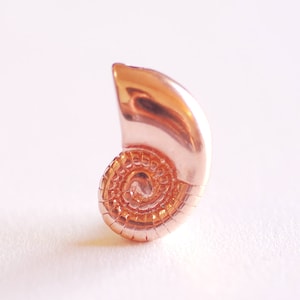 May include: A small, rose gold-colored seashell charm with a spiral design.