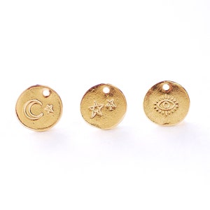 May include: Three gold-colored metal charms with different designs. The first charm features a crescent moon and a star. The second charm features two stars. The third charm features an eye with a circle around it.