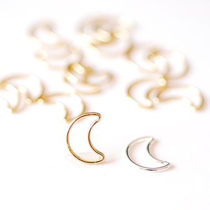 以下が含まれることがあります： 金色の三日月形のチャームのグループのクローズアップ。手前に銀色の三日月形のチャームが1つある。