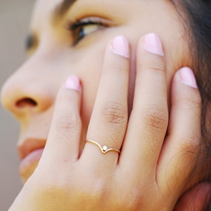 May include: A close-up of a woman's hand wearing a delicate gold ring with a small diamond. The ring is a simple, V-shaped band with a single diamond in the center.