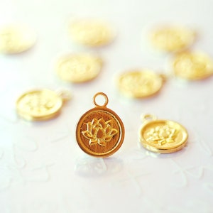 May include: Gold-coloured metal pendants featuring a lotus flower design. The pendants are circular with a small loop at the top for attaching to a chain. The background is white.