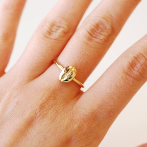 May include: A gold ring featuring a seashell design. The ring is worn on a finger.