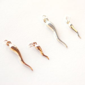 Puede incluir: Cuatro amuletos de cuerno en plata y oro, cada uno de un tamaño diferente. Los amuletos están sobre un fondo blanco.