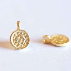 Peut inclure: Deux breloques en métal de couleur dorée avec un motif circulaire. Les breloques ont une surface texturée et une petite boucle en haut pour les attacher à un collier ou un bracelet.