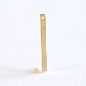 Puede incluir: Una barra de metal de color dorado con un pequeño agujero en el centro. La barra mide aproximadamente 2,5 cm de largo y 0,3 cm de ancho.