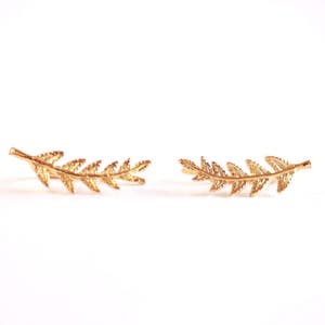 May include: A pair of gold leaf ear cuffs. The cuffs are shaped like a branch of leaves and are curved to fit the ear.