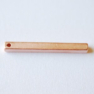 Peut inclure: Un pendentif en forme de barre en or rose avec un petit trou en haut pour attacher une chaîne ou une ficelle.