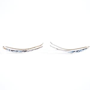 May include: A pair of silver ear cuffs with a textured, curved design. The cuffs are simple and elegant.