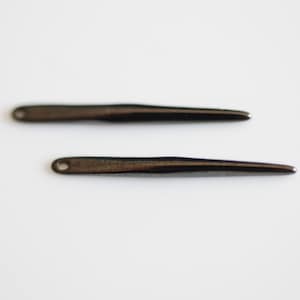 Puede incluir: Dos agujas de crochet de metal negro con puntas puntiagudas.