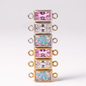 May include: A vertical stack of six rectangular jewelry connectors. The top three are silver-toned with pink, clear, and iridescent opal-like stones. The bottom three are gold-toned with pink, clear, and iridescent opal-like stones, each with side loops.
