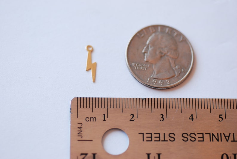 May include: Gold-toned lightning bolt charm pendant with a loop at the top. The charm is about 1 inch tall and is shown next to a US quarter for size comparison.