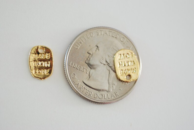 May include: Two gold-coloured metal tags with text. The tag on the left says "Made with Love". The tag on the right says "Love Pizza Now". The tags are shown next to a US quarter.