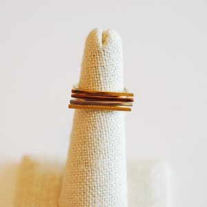 May include: A stack of four gold, silver, and copper rings on a fabric ring display stand.