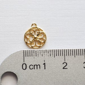 May include: Gold-toned metal charm with a circular, openwork design. The charm is about 1 cm in diameter and has a loop at the top for attaching to a necklace or bracelet.