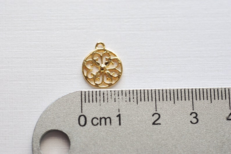 May include: Gold-toned metal charm with a circular, openwork design. The charm is about 1 cm in diameter and has a loop at the top for attaching to a necklace or bracelet.