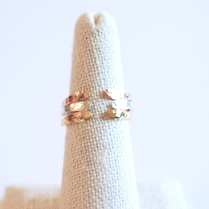 May include: A set of three hammered metal rings in gold, silver, and rose gold tones. The rings are stacked on a fabric ring holder.