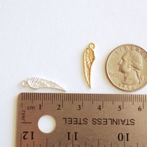 May include: Two gold-colored metal angel wings, one silver-colored metal angel wing, and a US quarter for size comparison. The wings are approximately 1 inch in length.