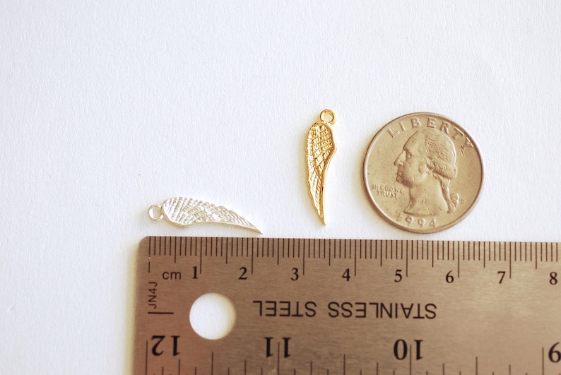 May include: Two gold-colored metal angel wings, one silver-colored metal angel wing, and a US quarter for size comparison. The wings are approximately 1 inch in length.