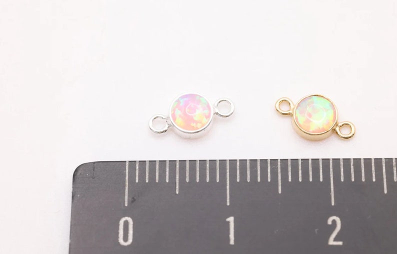 May include: Two round opal connector charms, one silver and one gold, with a 1 cm diameter. The charms have two jump rings for attaching to jewelry.