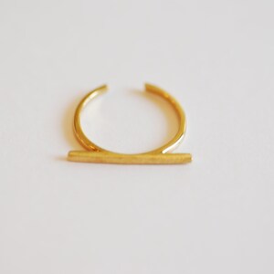 May include: A gold-toned ring with a thin, horizontal bar across the top.