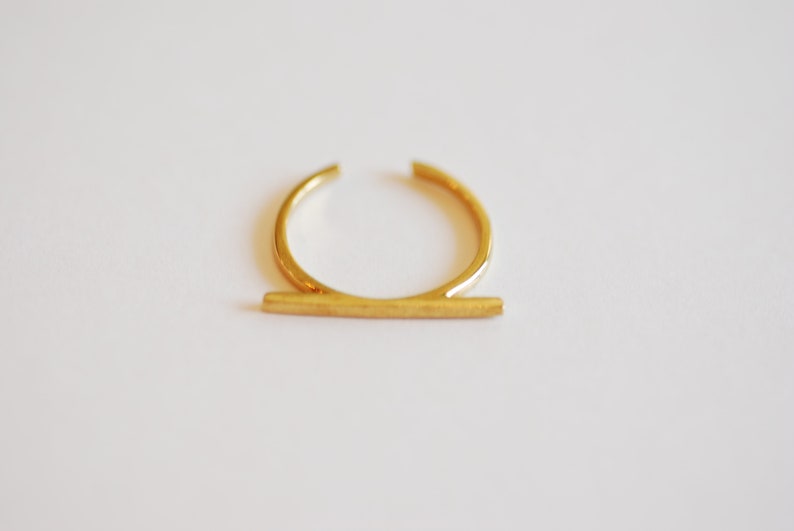 May include: A gold-toned ring with a thin, horizontal bar across the top.