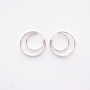 May include: A pair of silver hoop earrings with a double circle design.