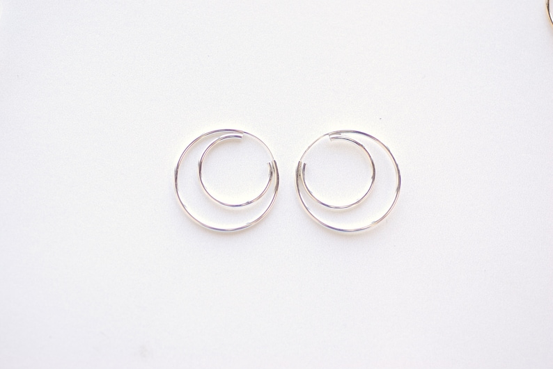 May include: A pair of silver hoop earrings with a double circle design.