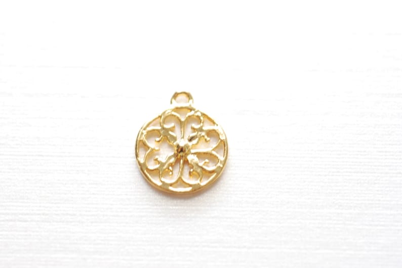 May include: Gold-toned metal pendant with a circular, openwork design featuring a floral pattern.