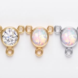 May include: Three jewelry connectors featuring circular settings with three attached jump rings. The first is gold-toned with a clear faceted stone, the second is gold-toned with an iridescent opal-like stone, and the third is silver-toned with an iridescent opal-like stone.