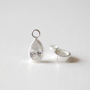 May include: Two silver teardrop-shaped charms with clear cubic zirconia stones. The charms have a loop at the top for attaching to a necklace or bracelet.