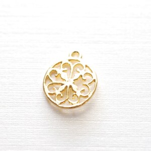 May include: Gold-toned metal ornament charm with a delicate, intricate design. The charm is round and features a cutout pattern of swirls and loops.