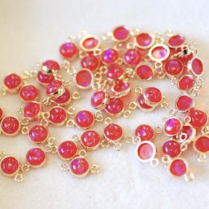 May include: A group of pink opal connector charms with gold-toned metal loops. The charms are scattered on a white surface.
