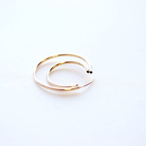 May include: Two gold hoop earrings, one slightly larger than the other, are shown on a white background.