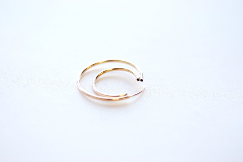May include: Two gold hoop earrings, one slightly larger than the other, are shown on a white background.