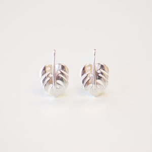 May include: A pair of silver earrings shaped like monstera leaves. The earrings are simple and elegant, and would make a great gift for any plant lover.