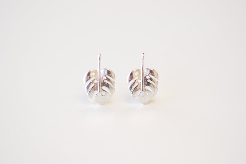 May include: A pair of silver earrings shaped like monstera leaves. The earrings are simple and elegant, and would make a great gift for any plant lover.