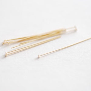 Puede incluir: Primer plano de un montón de alfileres de cabeza dorados. Los alfileres miden aproximadamente 2,5 cm de largo y tienen una cabeza pequeña y plana.