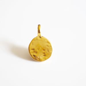 Puede incluir: Pendiente de encanto de color dorado con un diseño circular martillado y texturizado. El pendiente tiene un bucle en la parte superior para sujetarlo a un collar o pulsera.