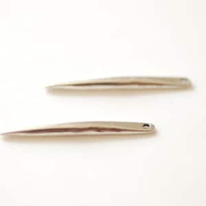 Puede incluir: Dos herramientas de metal de color plateado en forma de aguja con extremos puntiagudos. Las herramientas están sobre una superficie blanca.