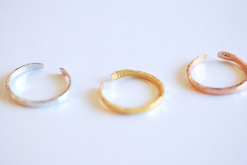 May include: Three hammered metal rings in silver, gold, and rose gold.