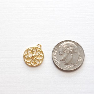 May include: A gold-colored metal charm with a circular, intricate design. The charm is about the size of a US dime.