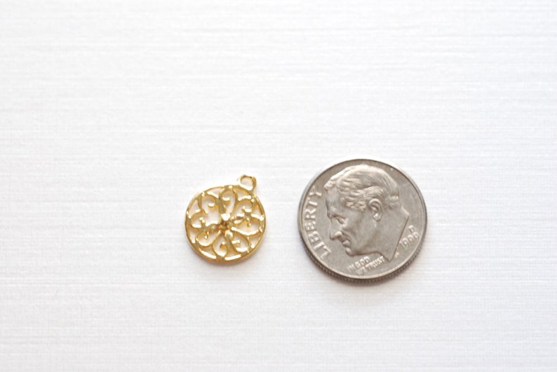 May include: A gold-colored metal charm with a circular, intricate design. The charm is about the size of a US dime.