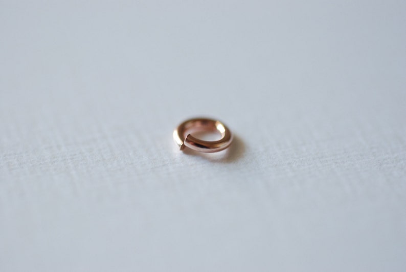 May include: A small, rose gold jump ring. This ring is a jewelry finding used for connecting chains, charms, and other jewelry components.