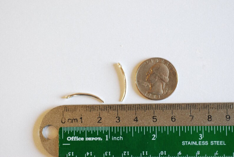 Op de afbeelding: Twee zilverkleurige metalen draadringen, elk met een diameter van ongeveer 2,5 cm, worden getoond naast een liniaal en een Amerikaanse kwart. De liniaal is gemarkeerd in zowel inches als centimeters.