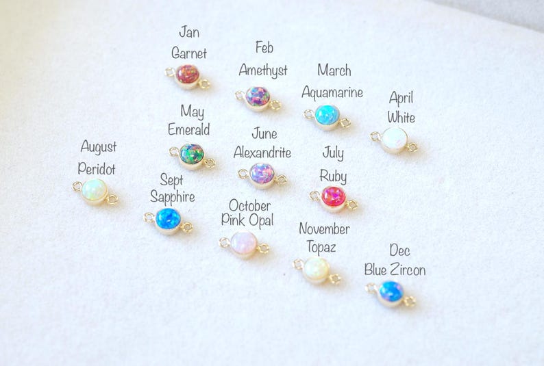 May include: Twelve small, round, gemstone charms with gold connectors. Each charm represents a different month of the year and features a different birthstone. The charms are arranged in a row, starting with January and ending with December.