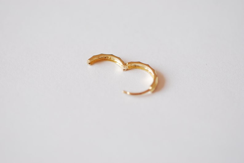 May include: A pair of gold hoop earrings with a geometric design.